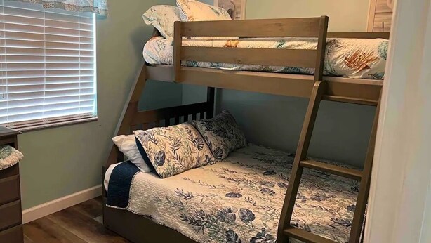 Una cama litera con ropa de cama floral, una ventana con persianas y un cuadro en la pared.