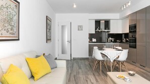 Une cuisine moderne avec des meubles blancs, un coin repas doté d’une table et de chaises blanches, et un canapé agrémenté de coussins jaunes.