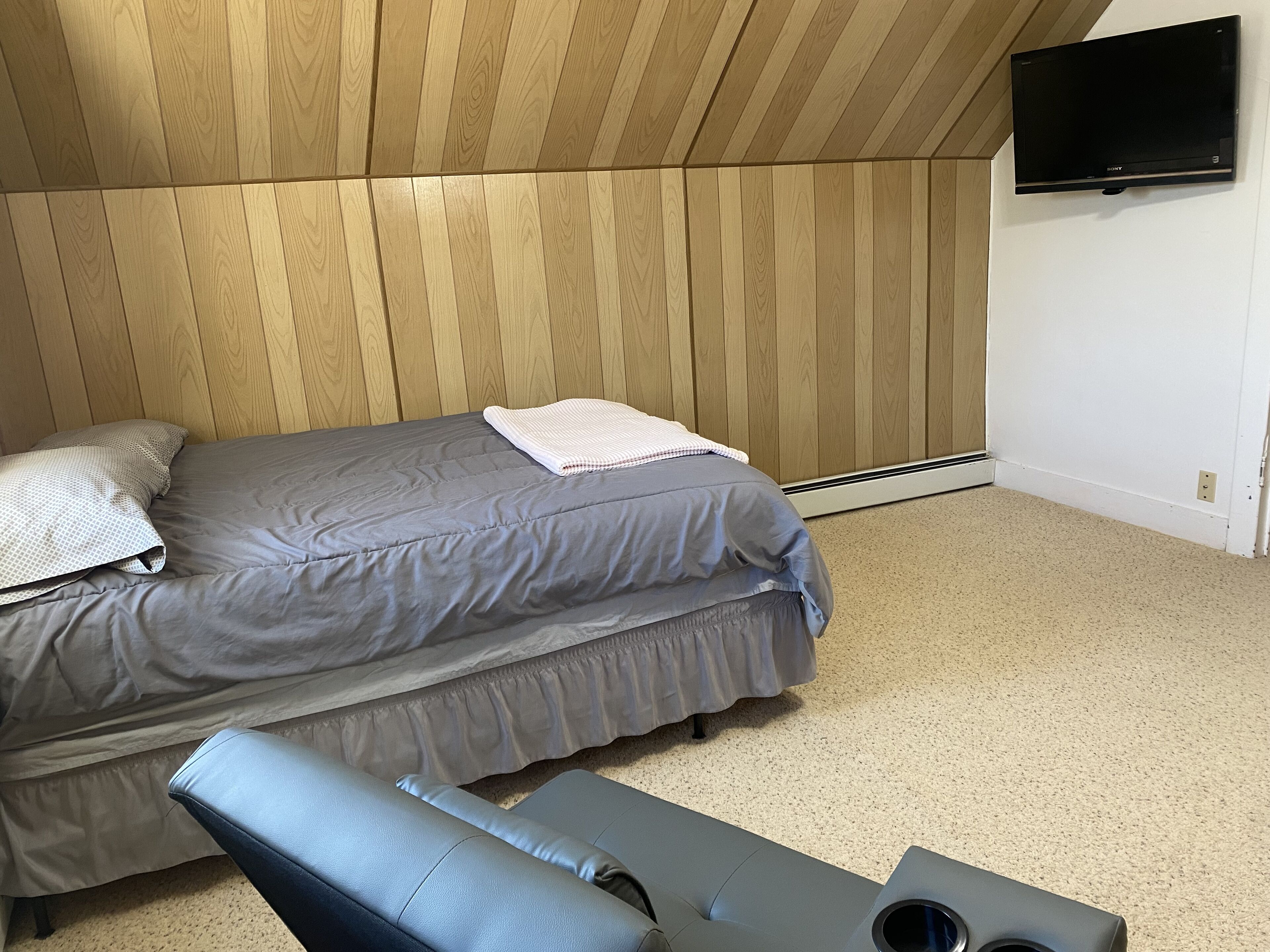 Un dormitorio con cama, almohadas, un banco y televisor montado en la pared.