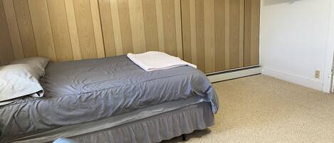 Un dormitorio con cama, almohadas, un banco y televisor montado en la pared.