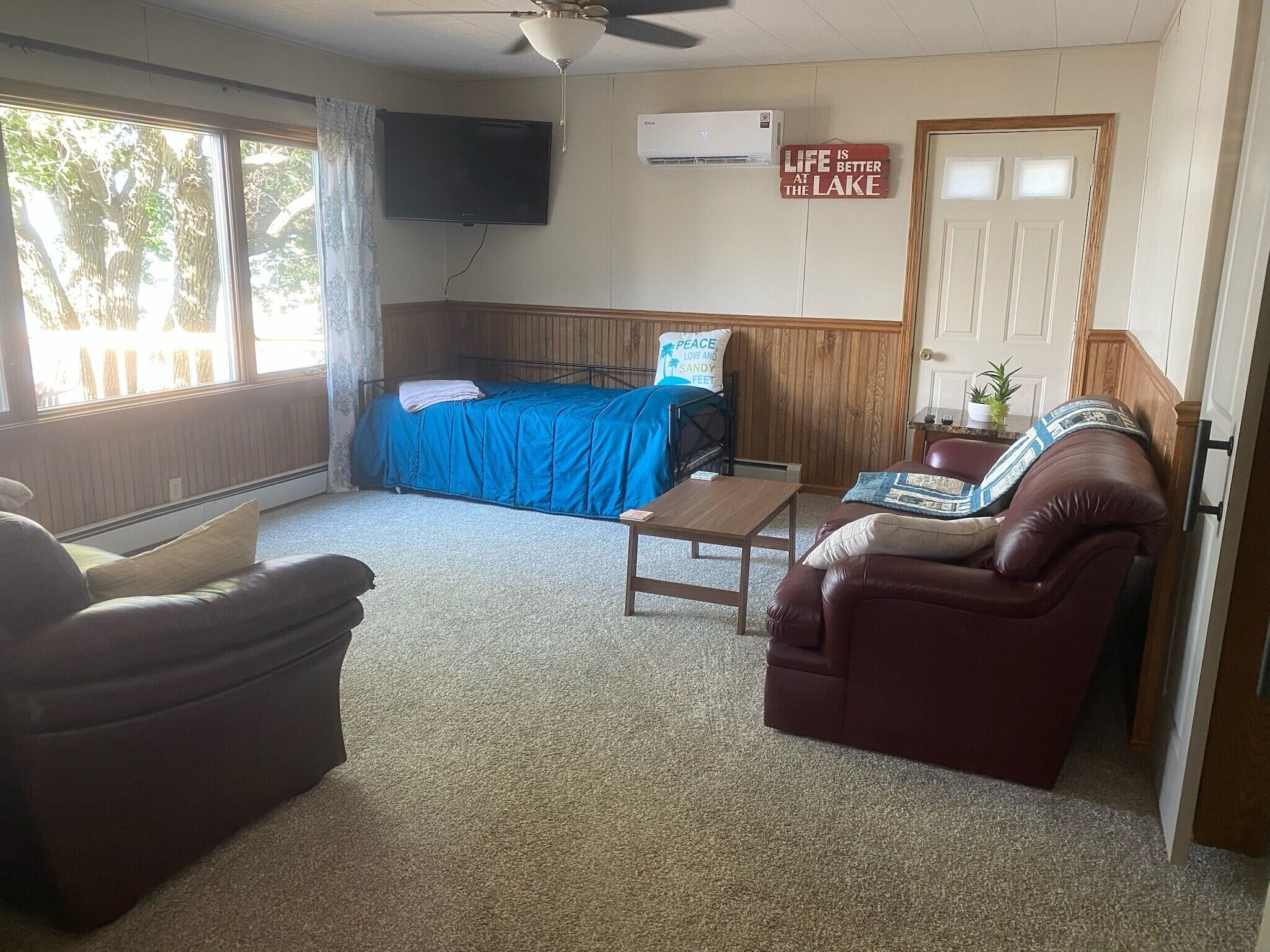 A room with a bed, a desk, a leather chair, a couch, a TV, and a door.