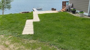 Un jardín cubierto de césped con un camino de hormigón que lleva a un muelle sobre un lago.