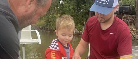 Un hombre y un niño en un muelle de madera junto al agua, sosteniendo una caña de pescar.