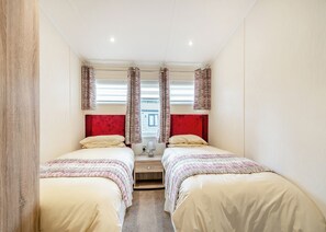 A bedroom with two beds, a nightstand, a lamp, and a window with curtains. - Country and modern cladded lodge. (Kirkcudbright)