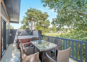 Un balcon extérieur avec un jacuzzi, des meubles en osier et une vue sur un quartier résidentiel.