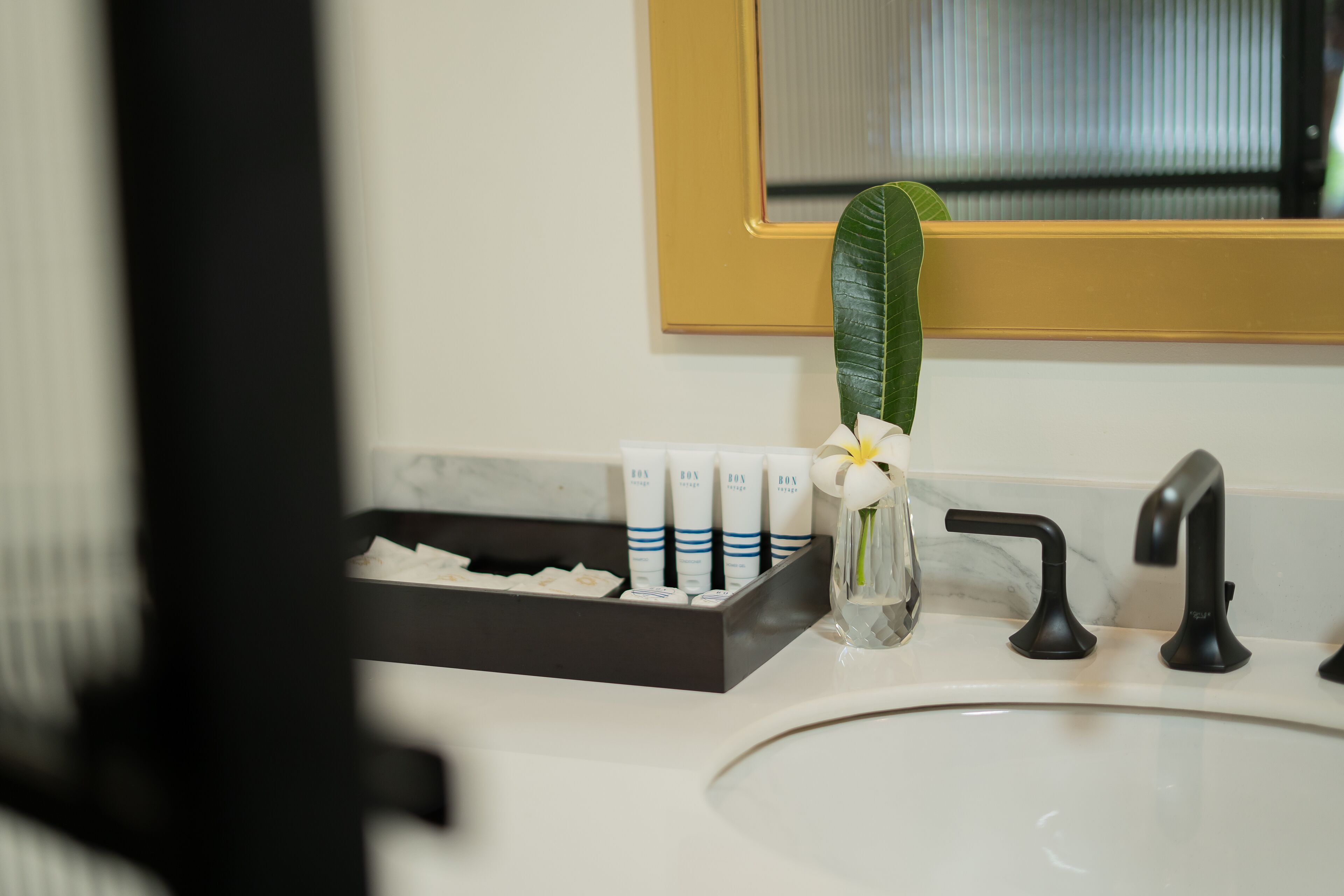 A bathroom sink with a black faucet, a white marble countertop, and a small vase with a white flower.