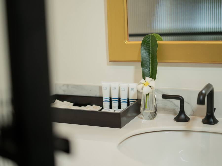 A bathroom sink with a black faucet, a white marble countertop, and a small vase with a white flower.