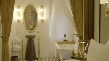 A bathroom with a large oval mirror, a sink with a bowl, a towel rack, and a vanity with a mirror and lights.