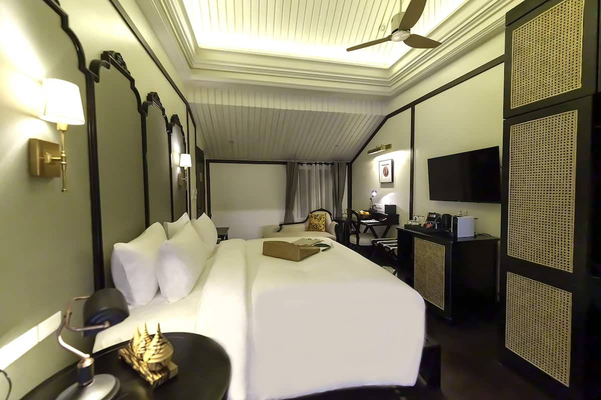 Ein Hotelzimmer mit einem großen Bett, einem Schreibtisch mit Computer, einem Fernseher und einem Deckenventilator.