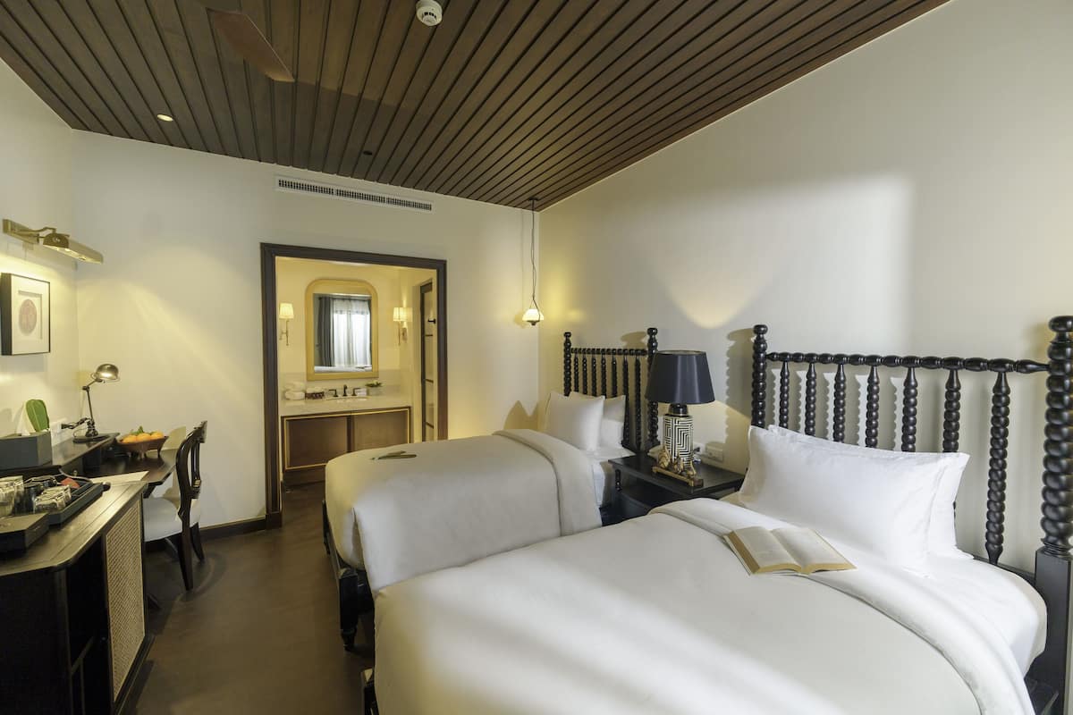 Ein Hotelzimmer mit zwei Betten, einem Schreibtisch, einem Stuhl, einem Nachttisch und einem Spiegel.