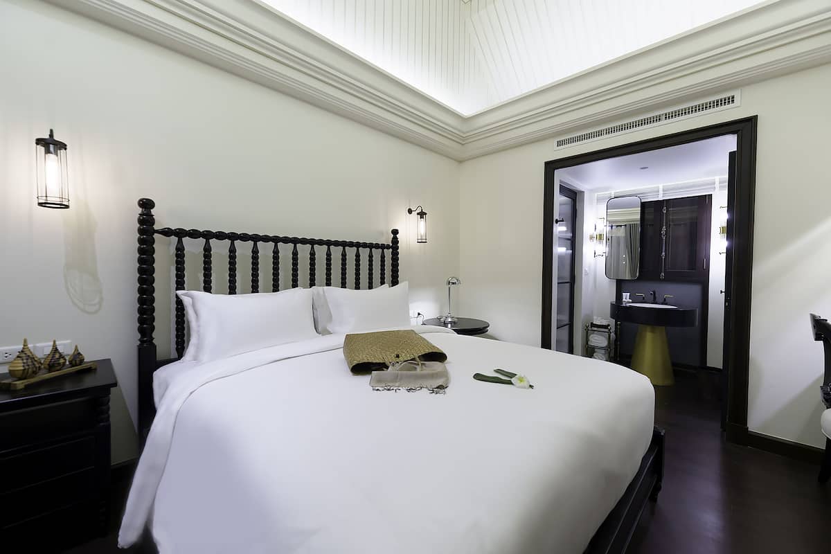 Ein Hotelzimmer mit einem großen Bett, einem Nachttisch, einer Lampe, einem Spiegel und einem durch eine geöffnete Tür einsehbaren Badezimmer.