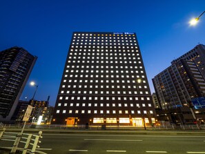 Un edificio de gran altura con varios pisos, probablemente un hotel o edificio de oficinas, que cuenta con una entrada destacada y ventanas iluminadas.