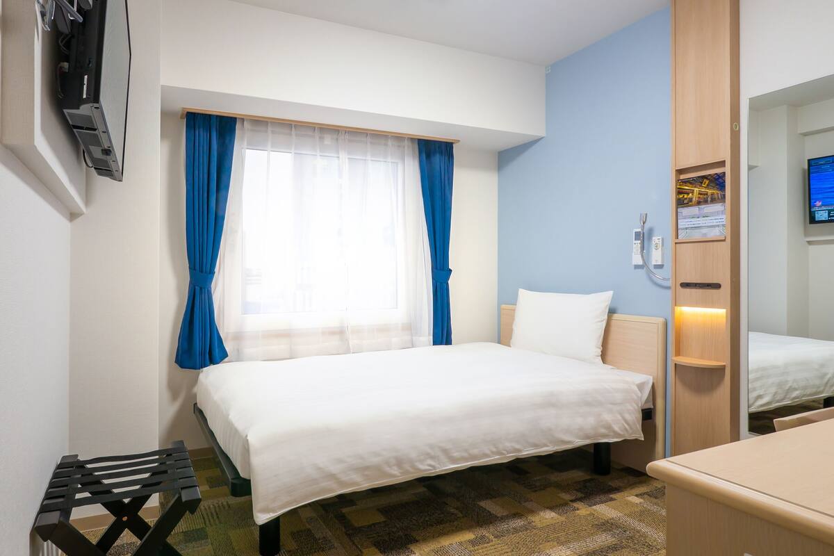 Una habitación de hotel con una cama, una mesita, un espejo y un televisor en la pared.