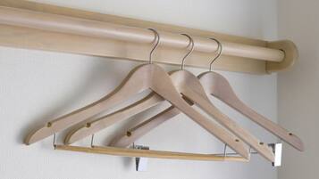 A wooden coat rack with three wooden hangers against a plain wall.