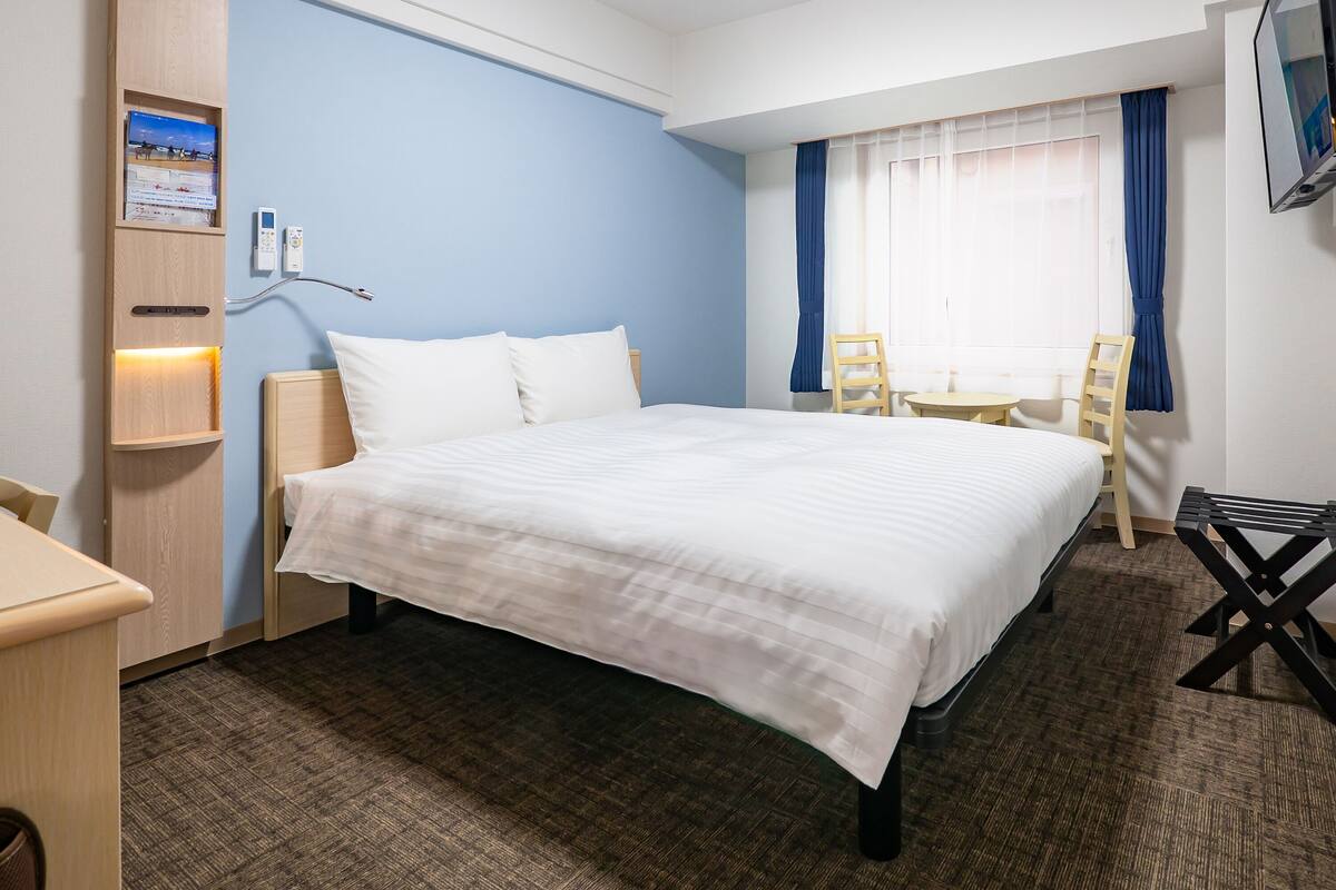 Una habitación de hotel con una cama grande, un escritorio, una silla, un televisor y una ventana con cortinas.