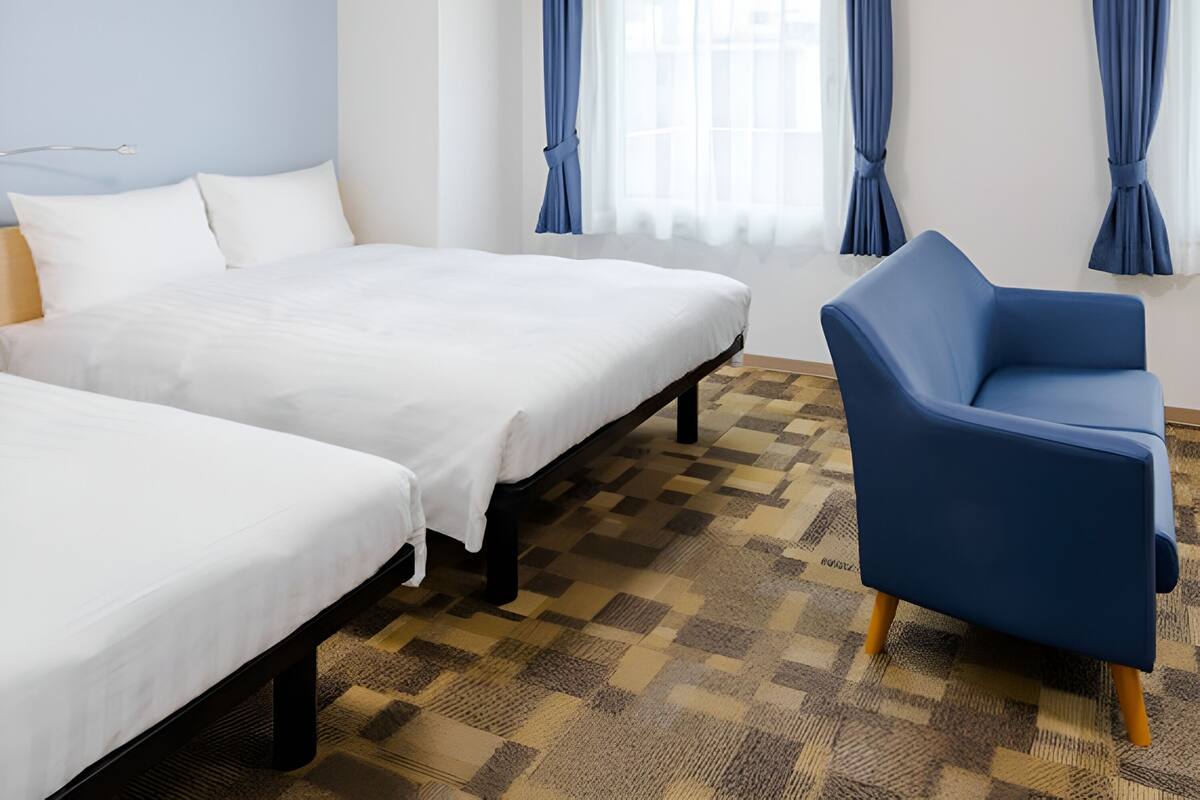 Una habitación de hotel con dos camas individuales, un sillón azul y piso a cuadros.