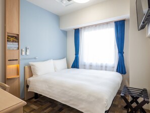 Una habitación de hotel con cama, escritorio, armario y ventana con cortinas.