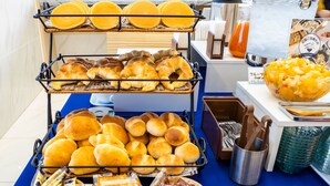 Un buffet de petit-déjeuner proposant une variété de viennoiseries, de pains et d’autres produits clairement identifiés, comme des petits pains au beurre, des crêpes, des croissants et une baguette moelleuse.