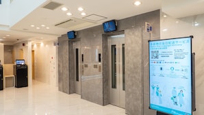 Un hall d’hôtel moderne doté d’un kiosque d’information numérique, d’ascenseurs et d’un sol carrelé, propre et élégant.