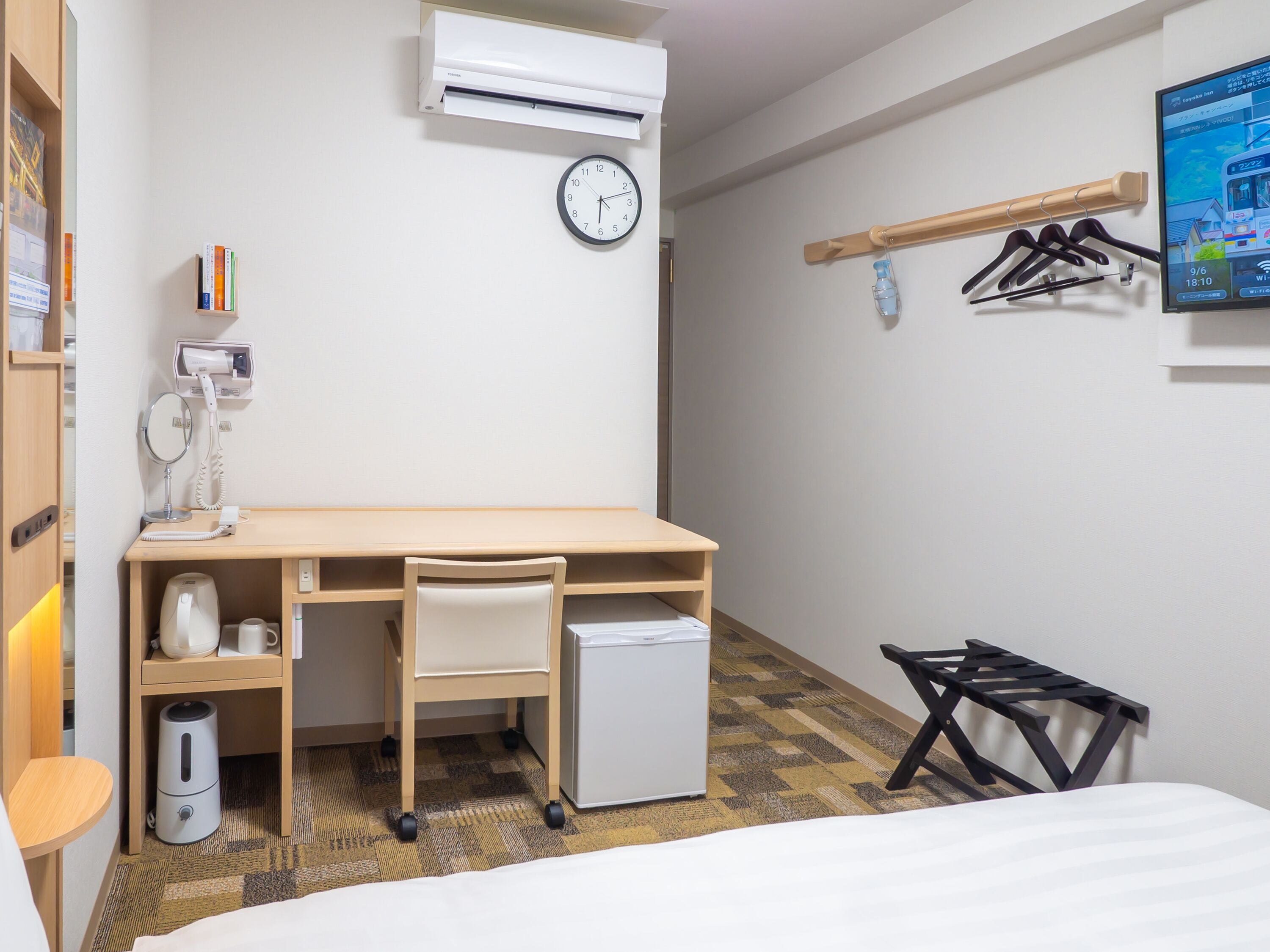 Une chambre d’hôtel équipée d’un bureau, d’une chaise, d’un climatiseur, d’une horloge et d’un petit réfrigérateur.