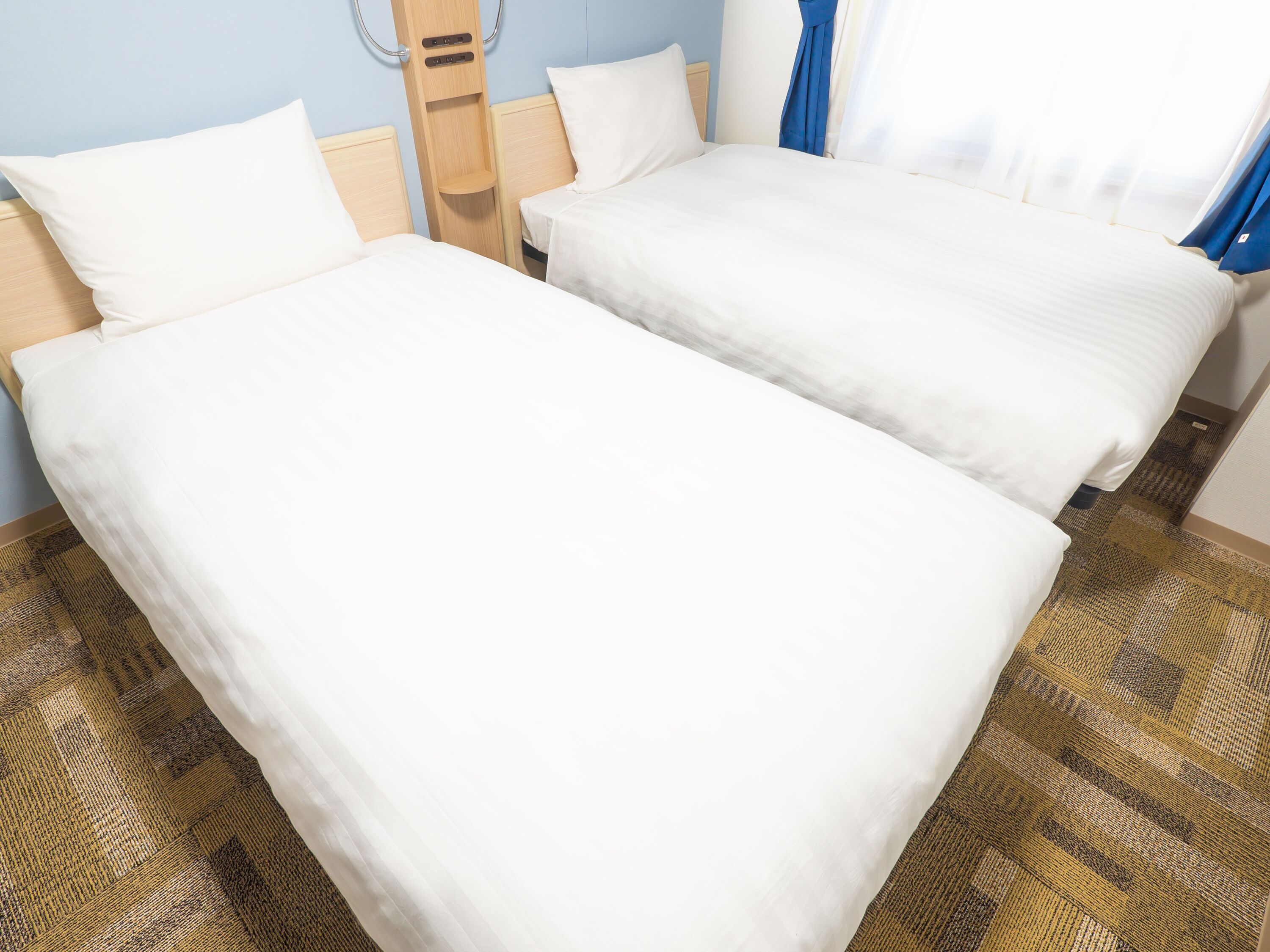 Two single beds with white linens in a room with a patterned carpet and light blue walls.