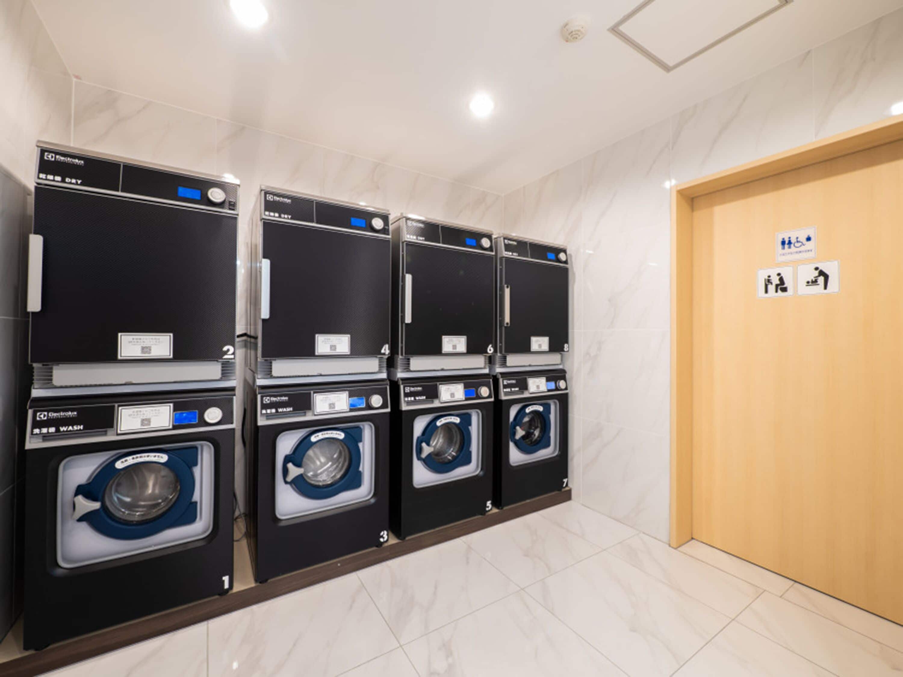 A laundry facility with multiple washing machines, a wooden door, and a sign indicating facilities for the disabled.
