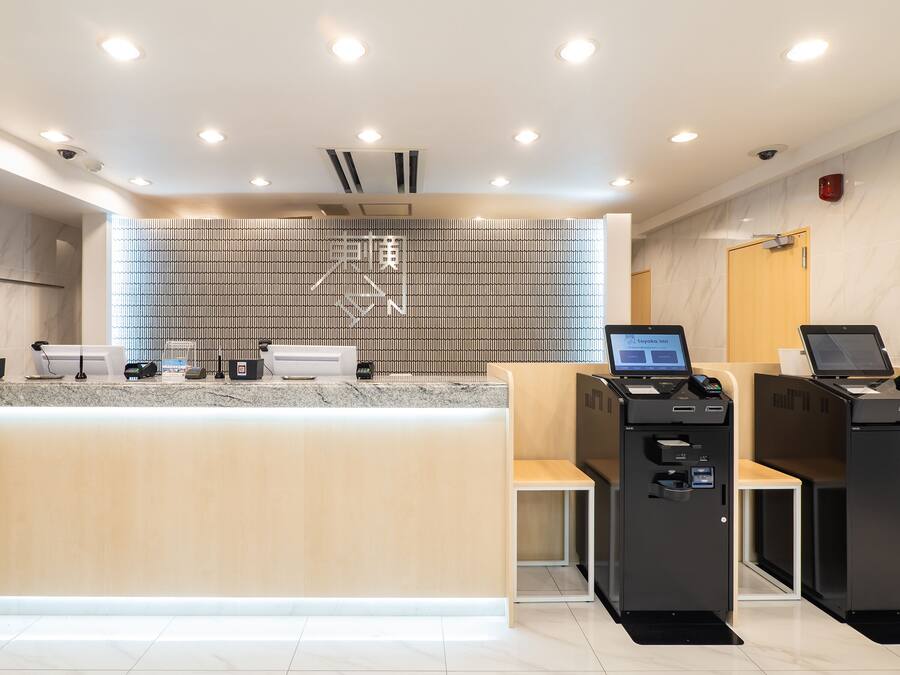 Uma área de recepção de hotel moderna, com balcão de mármore, estação de check-in digital e parede estampada.