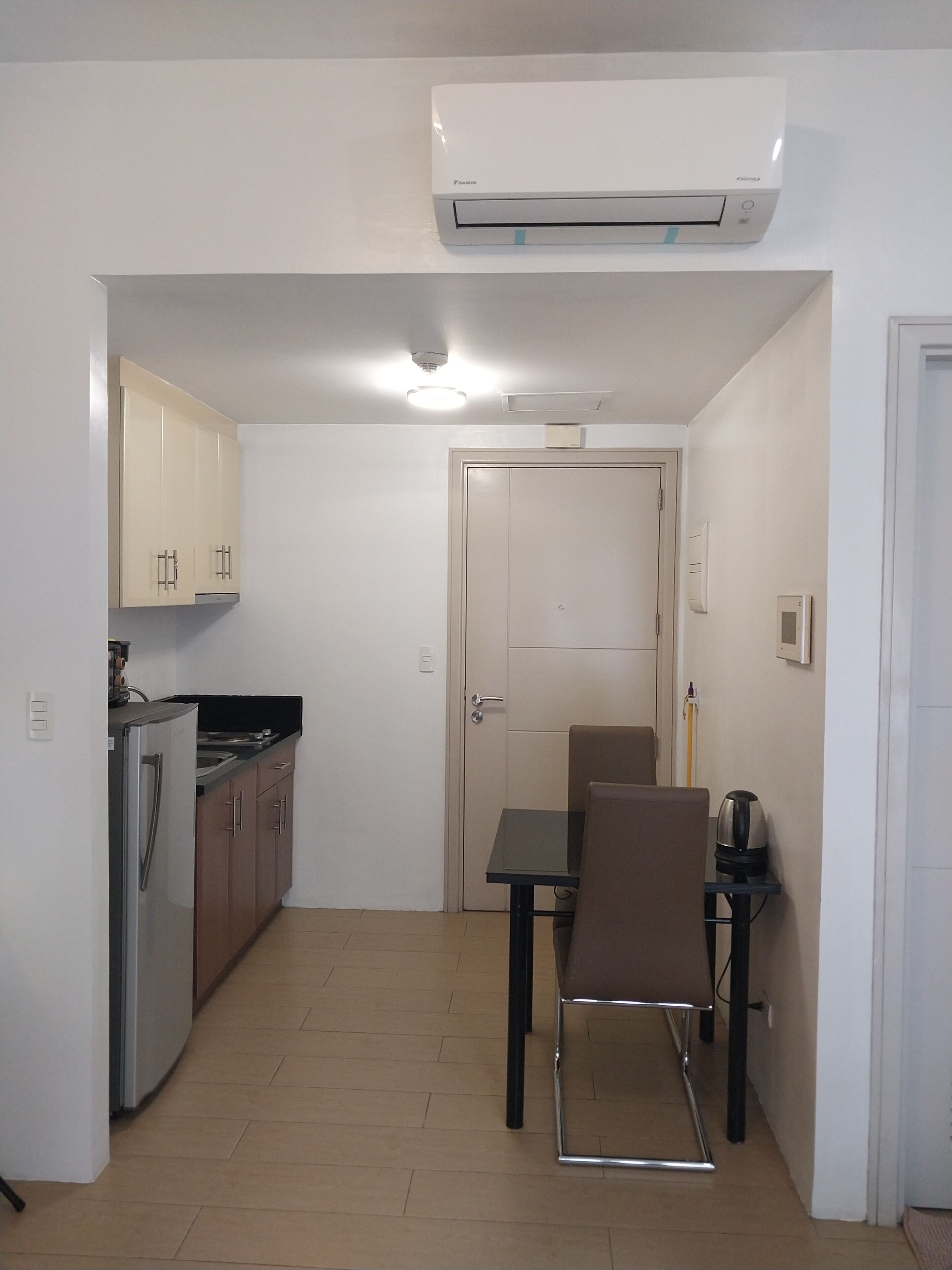 A compact kitchen with a refrigerator, stove, and cabinets, a dining table with chairs, and a white door.