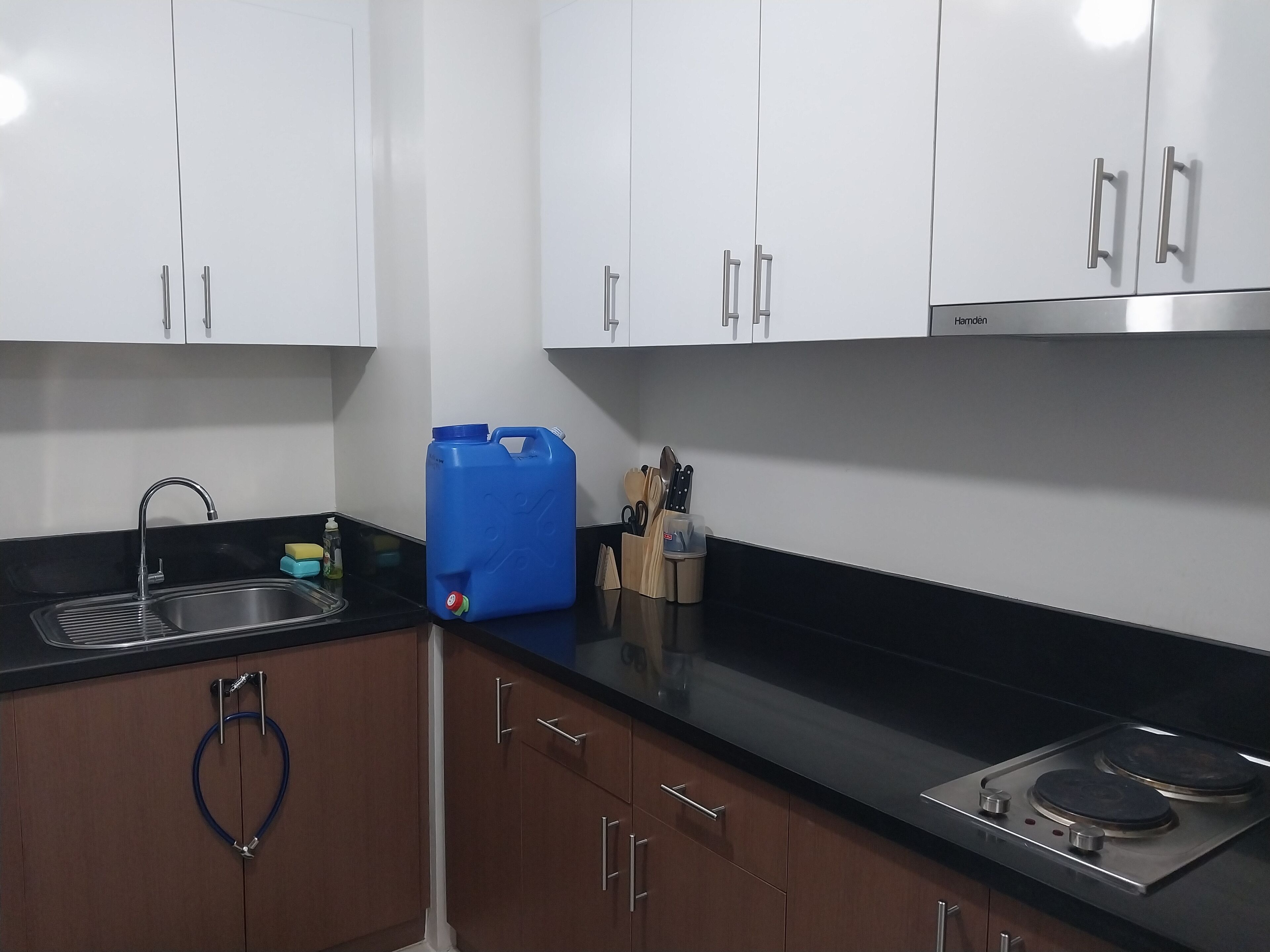 A modern kitchen with white cabinets, a black countertop, a stainless steel sink, and a stove.