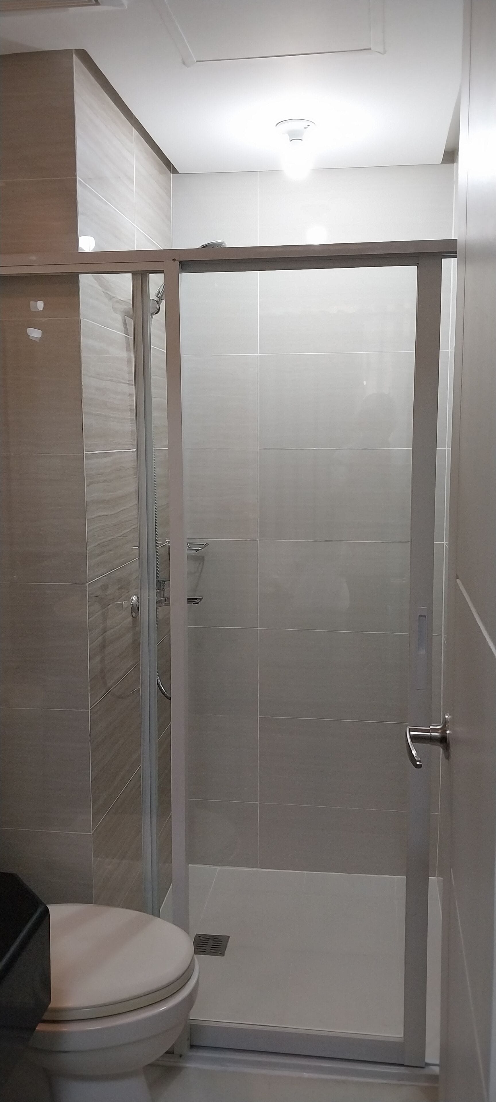 Ein Badezimmer mit Toilette, Duschkabine und Fliesenwänden.