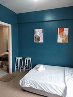 Een slaapkamer met een bed, twee witte krukken en kunst aan de muur.