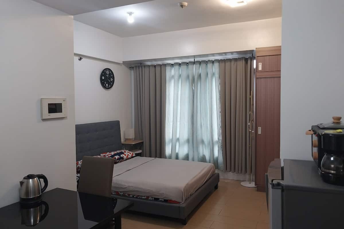A modern hotel room with a bed, a desk, a coffee maker, and a clock on the wall.