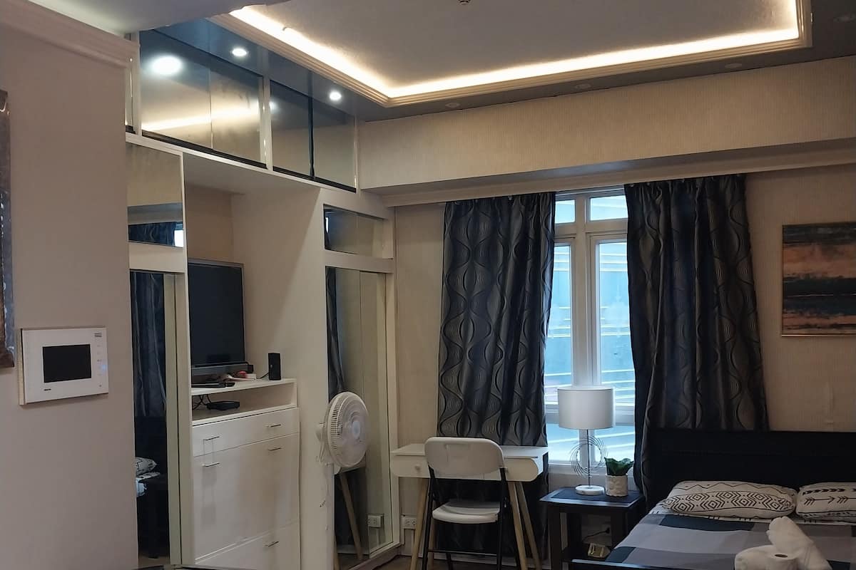 A hotel room with a bed, a desk, a chair, a small table, and a kitchenette area.