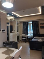 Ένα δωμάτιο ξενοδοχείου με ένα κρεβάτι, ένα γραφείο, μια καρέκλα, ένα μικρό τραπέζι και μια μικρή κουζίνα.