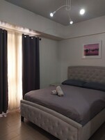 Quarto com cama, cortinas, mesa de cabeceira e um quadro na parede.