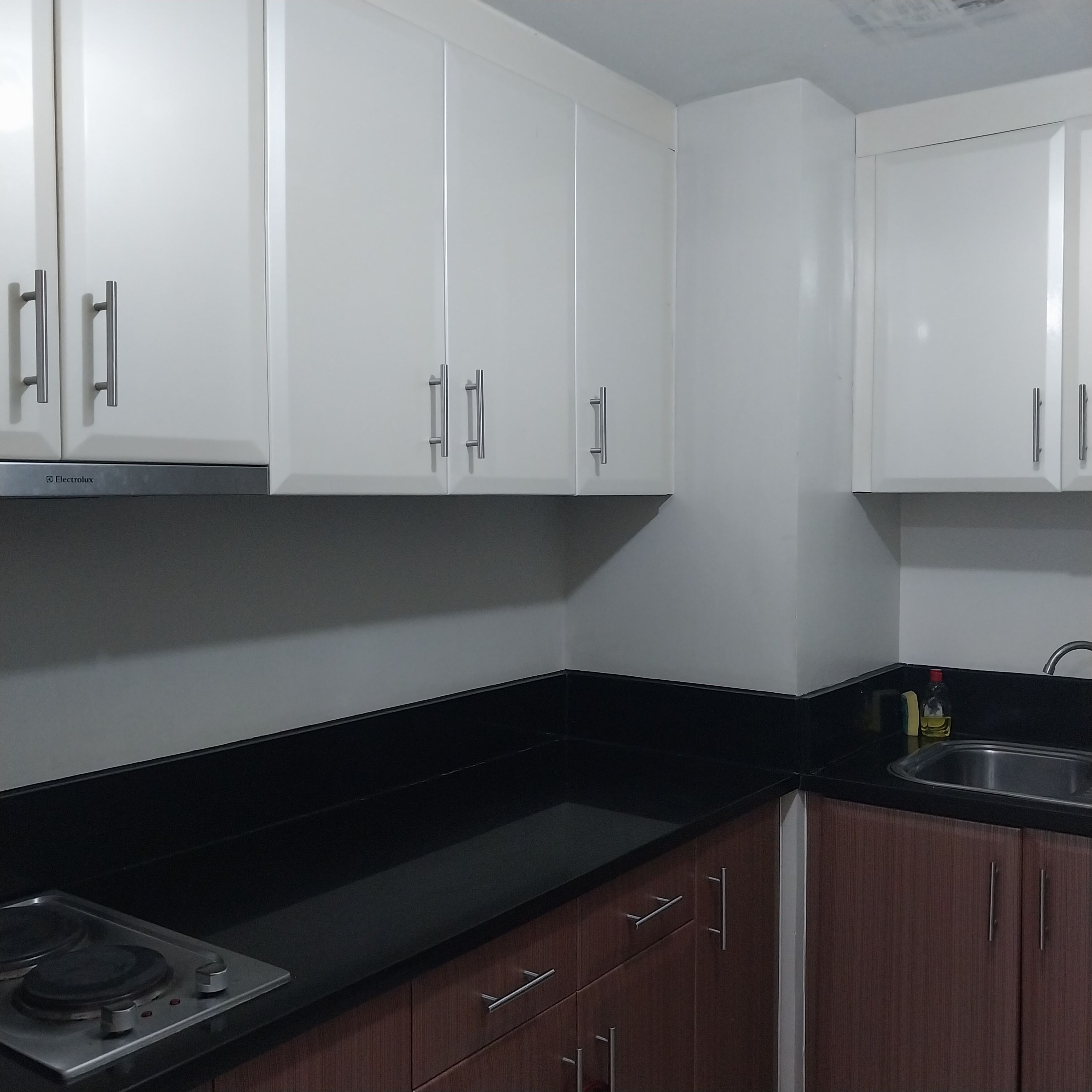 A kitchen with white cabinets, a black countertop, and a stainless steel sink.
