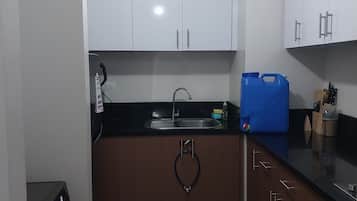 Una cocina moderna con armarios blancos, una encimera negra y un contenedor azul para almacenamiento.