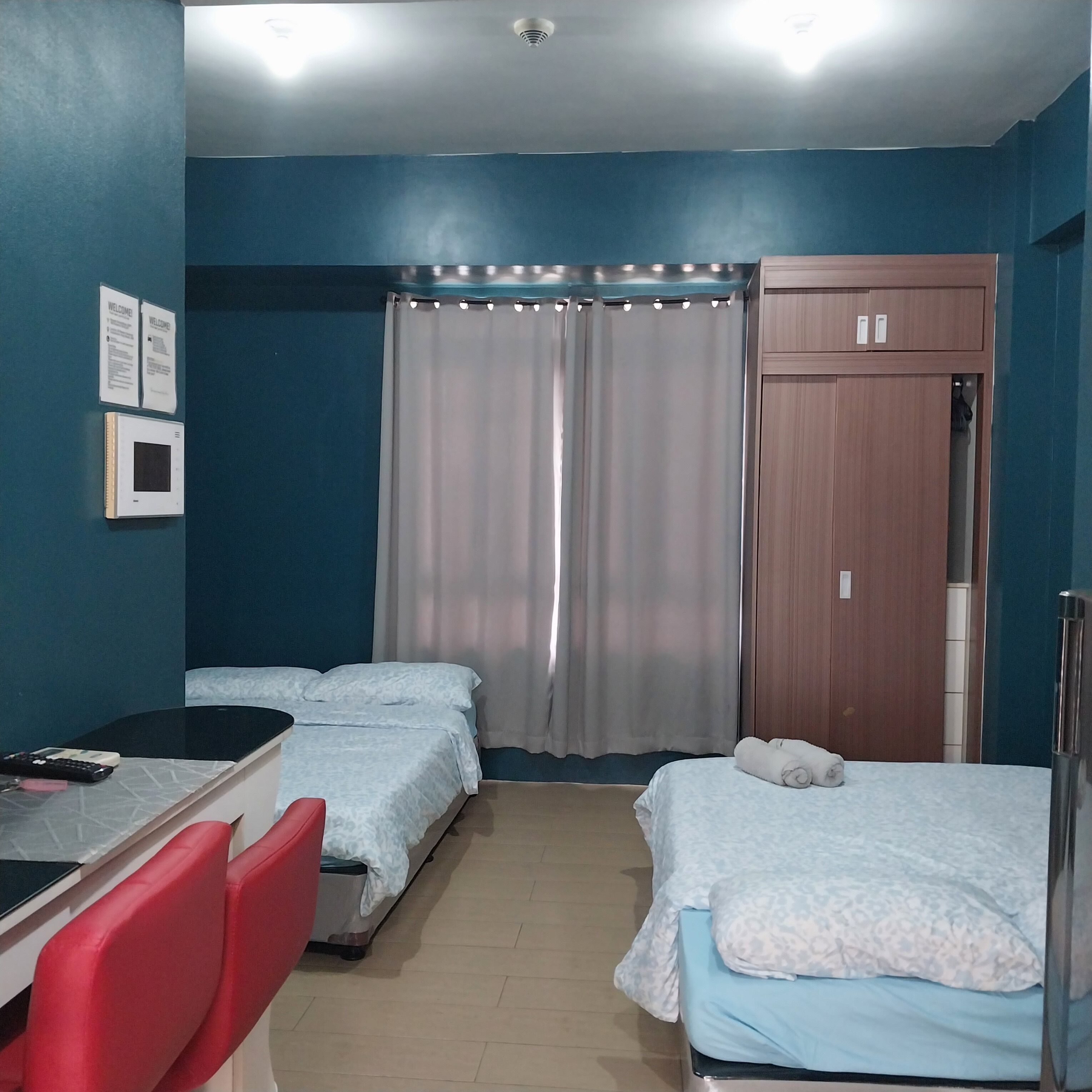 A hotel room with two beds, a desk with a chair, a wardrobe, and a curtain.