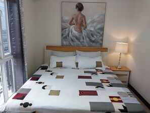 Une chambre d’hôtel avec un lit agrémenté d’une couvre-lit à motifs géométriques, d’une tête de lit en bois et d’un tableau représentant une personne dans l’eau, accroché au mur.