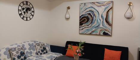 A living room with a sofa, a round wooden table, a clock, and a painting on the wall.