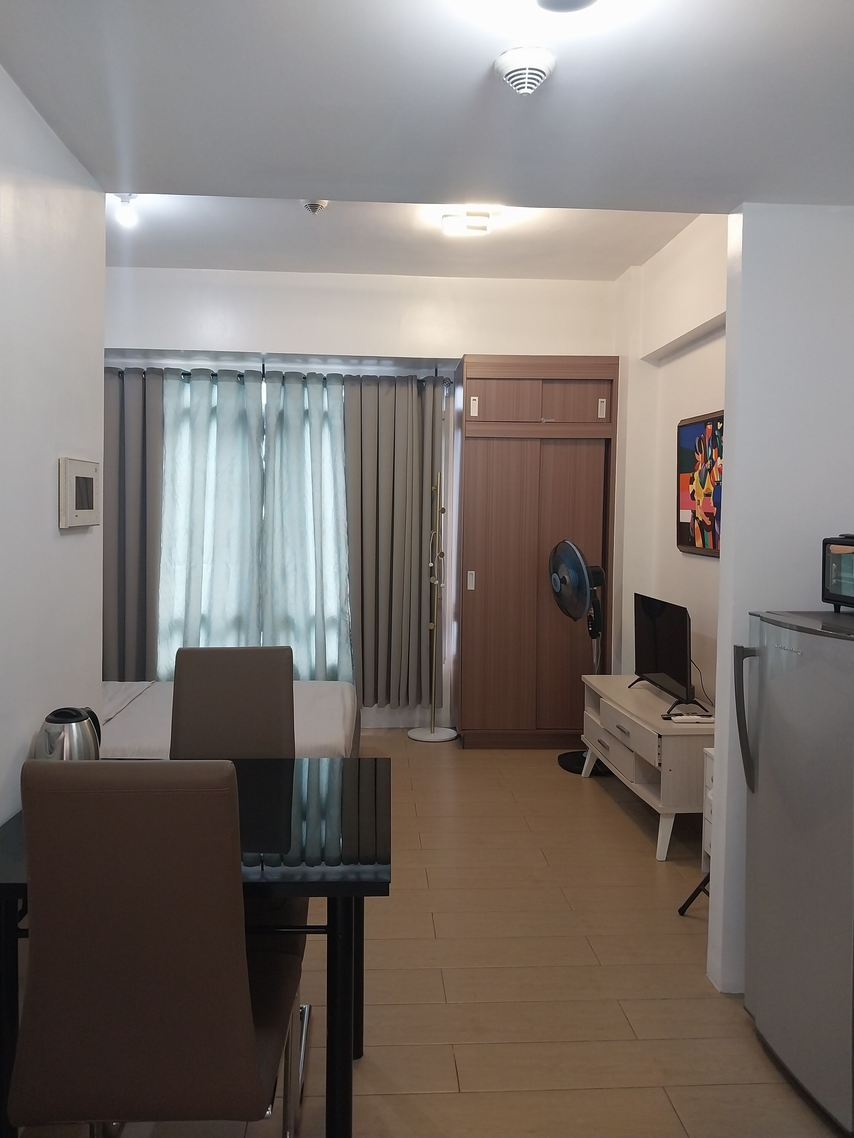 A modern living room with a dining area, a wooden cabinet, a TV, and a refrigerator.