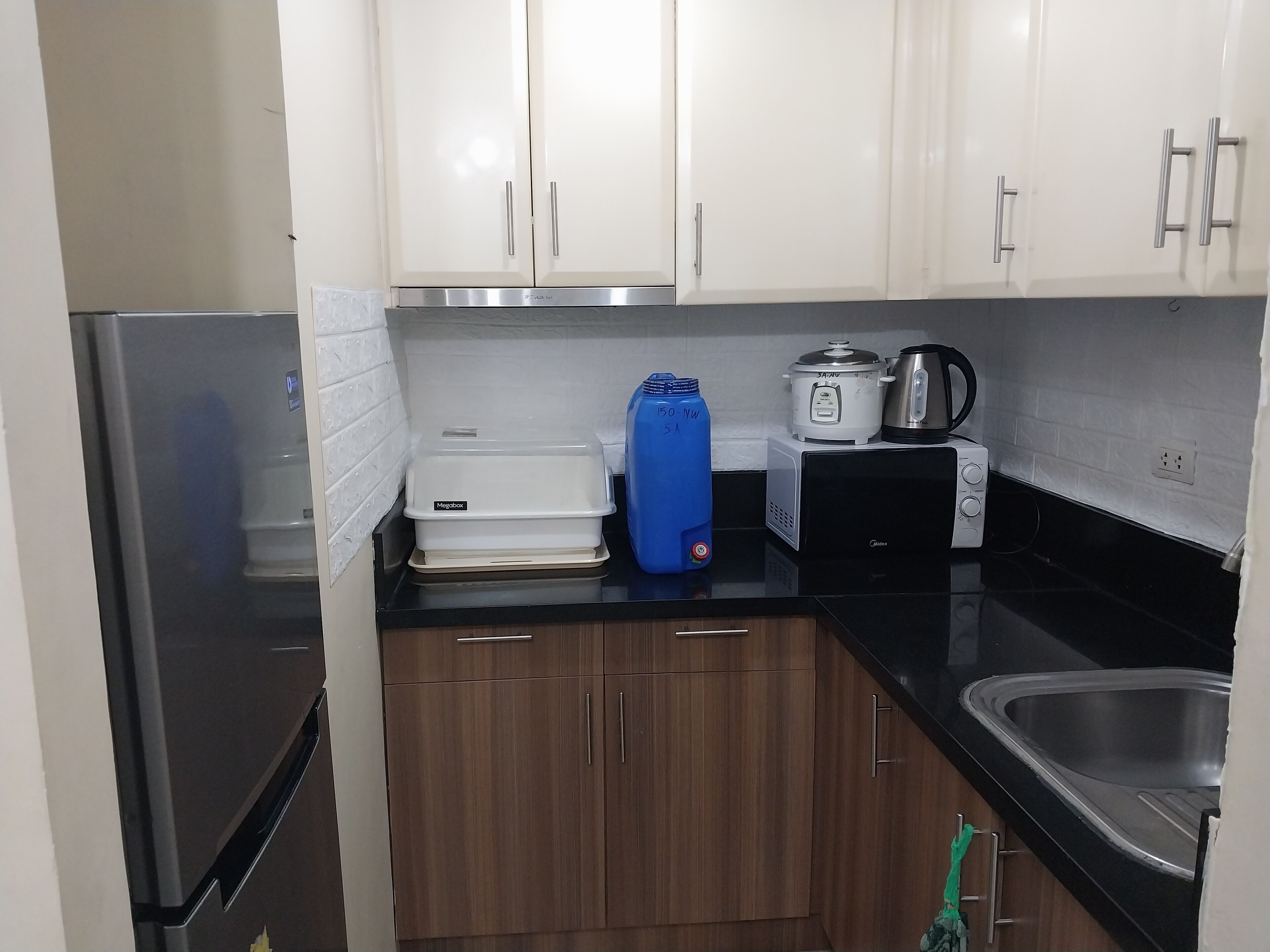 A compact kitchen with white cabinets, a black countertop, a stainless steel refrigerator, a white microwave, and a coffee maker.