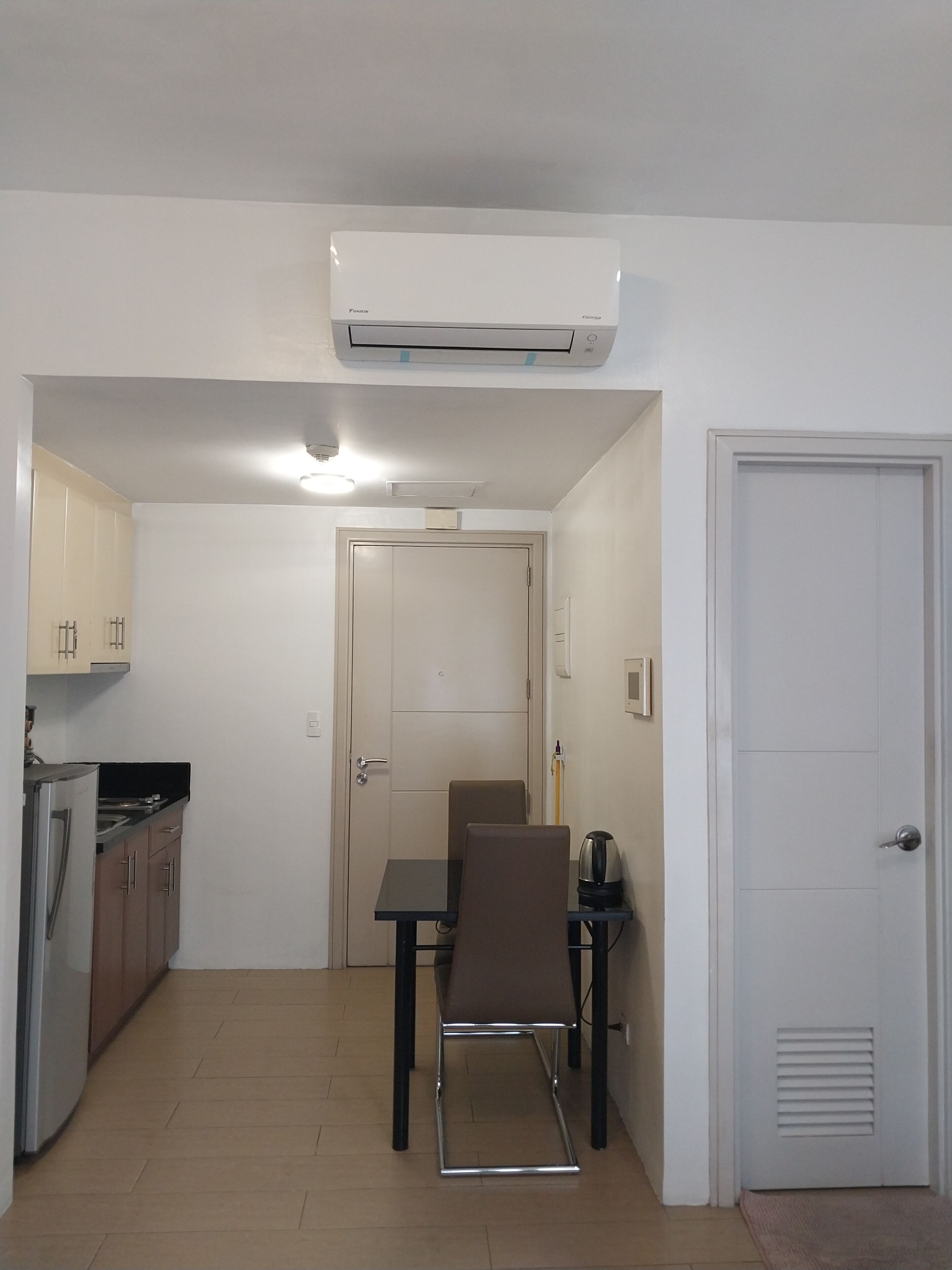 Cocina compacta con zona de comedor, que incluye una mesa y sillas, un refrigerador y un equipo de aire acondicionado.