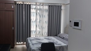 Un dormitorio con cama, cortinas, televisor y termostato.