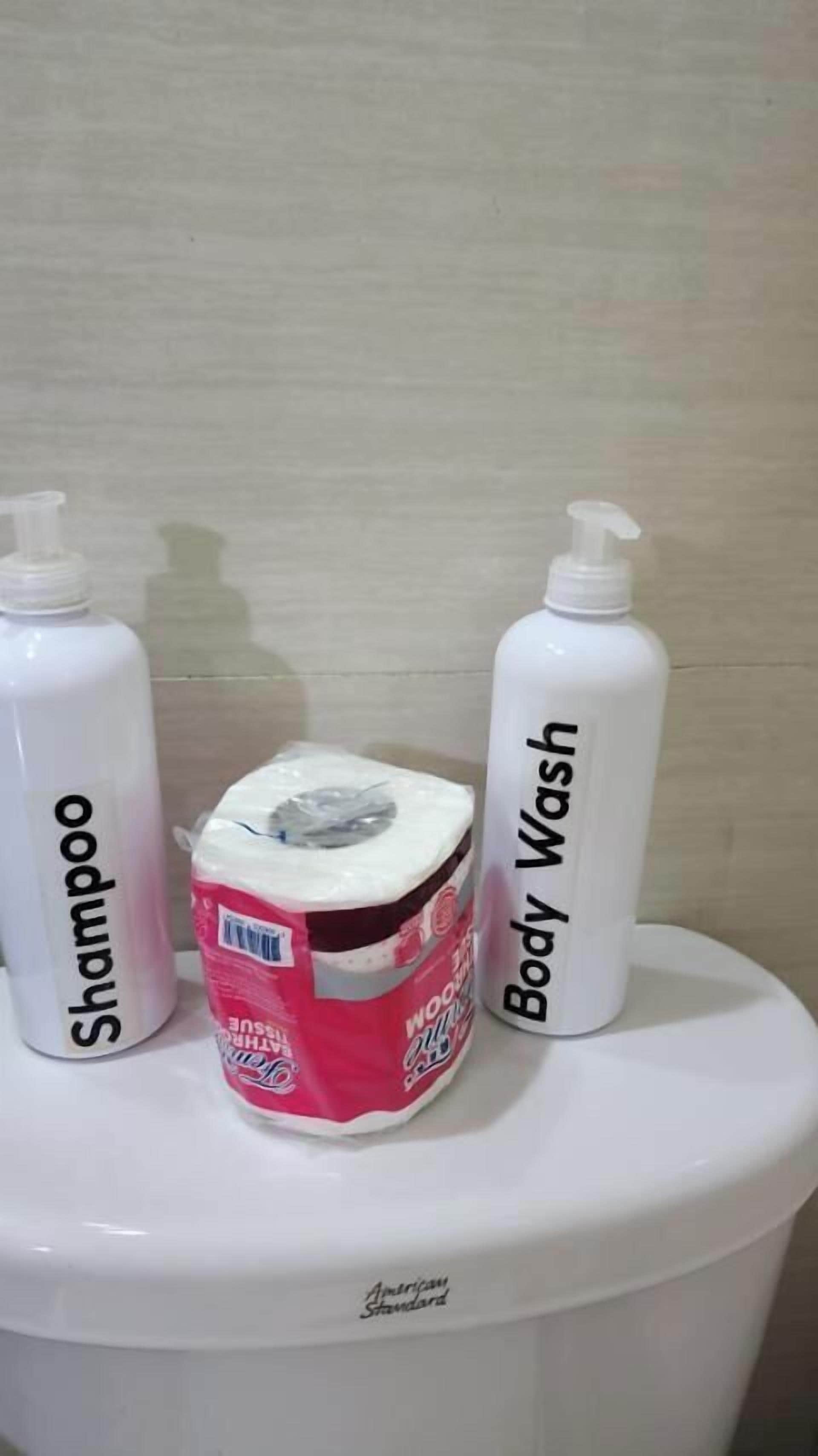 A toilet with three bottles: a shampoo bottle, a body wash bottle, and a pink bottle with a white cap.