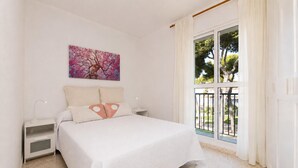 Un dormitorio con cama, mesitas de noche, un cuadro y vistas al exterior.
