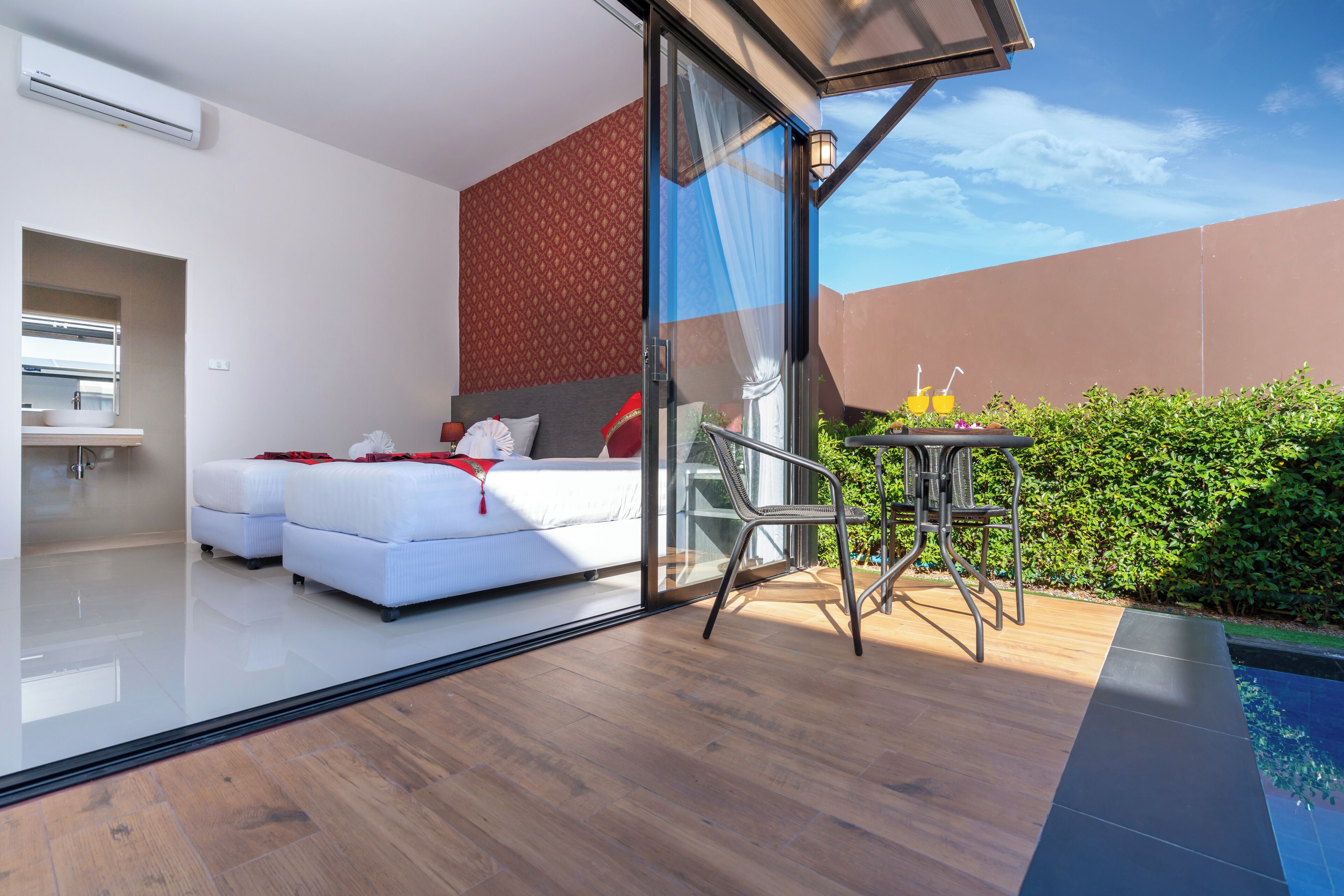 Une chambre moderne avec une porte vitrée donnant sur un balcon, un lit blanc et une petite table avec des boissons.
