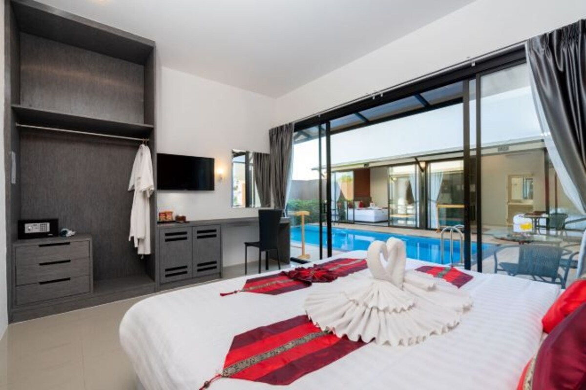 A hotel room with a large bed, a desk, a chair, a TV, and a view of a swimming pool.