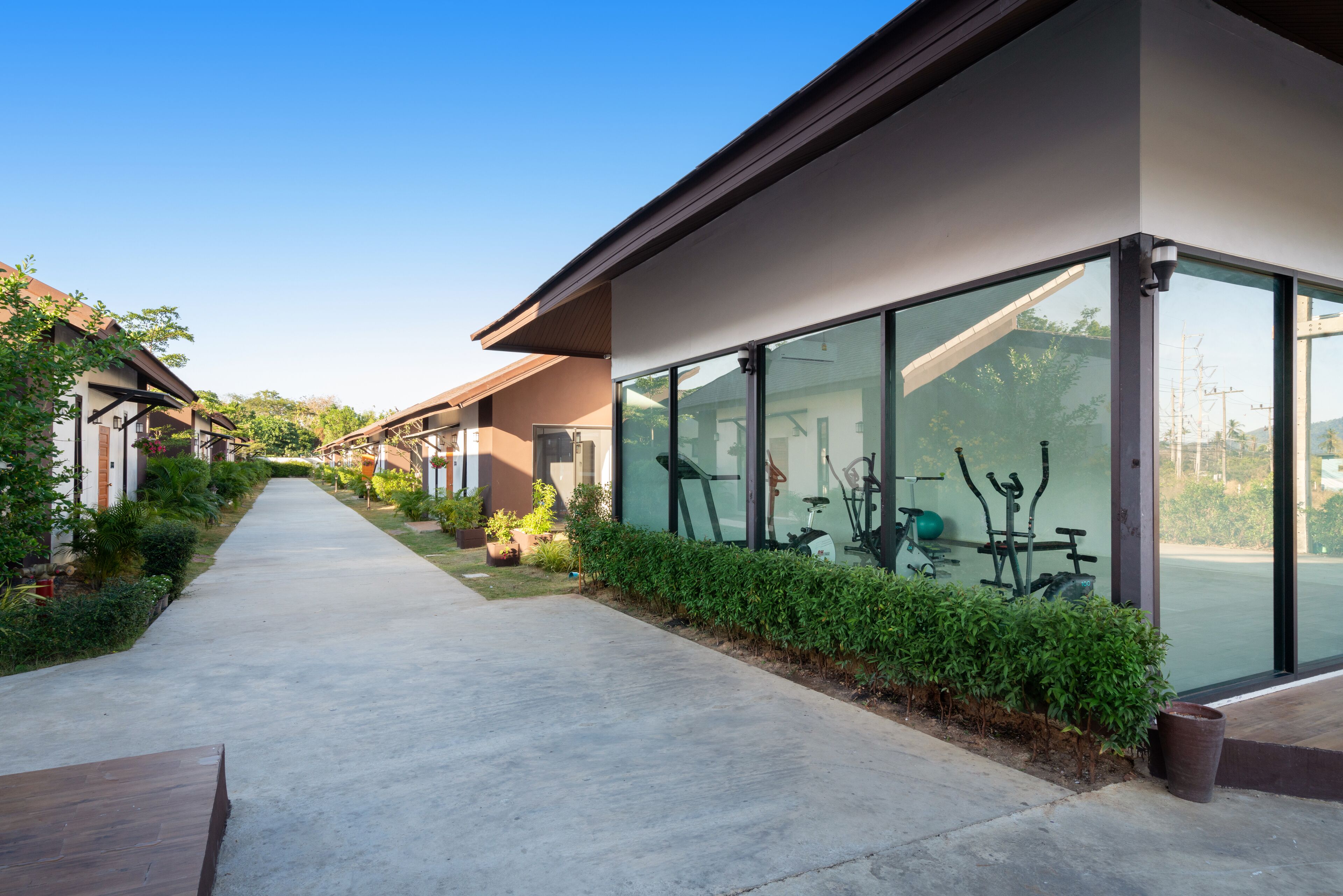 Un edificio moderno con amplios ventanales de vidrio, un sendero de concreto y equipo de ejercicio al aire libre.