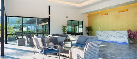 Un vestíbulo moderno con mobiliario de mimbre, un mostrador de recepción y grandes ventanales que ofrecen vistas al exterior.